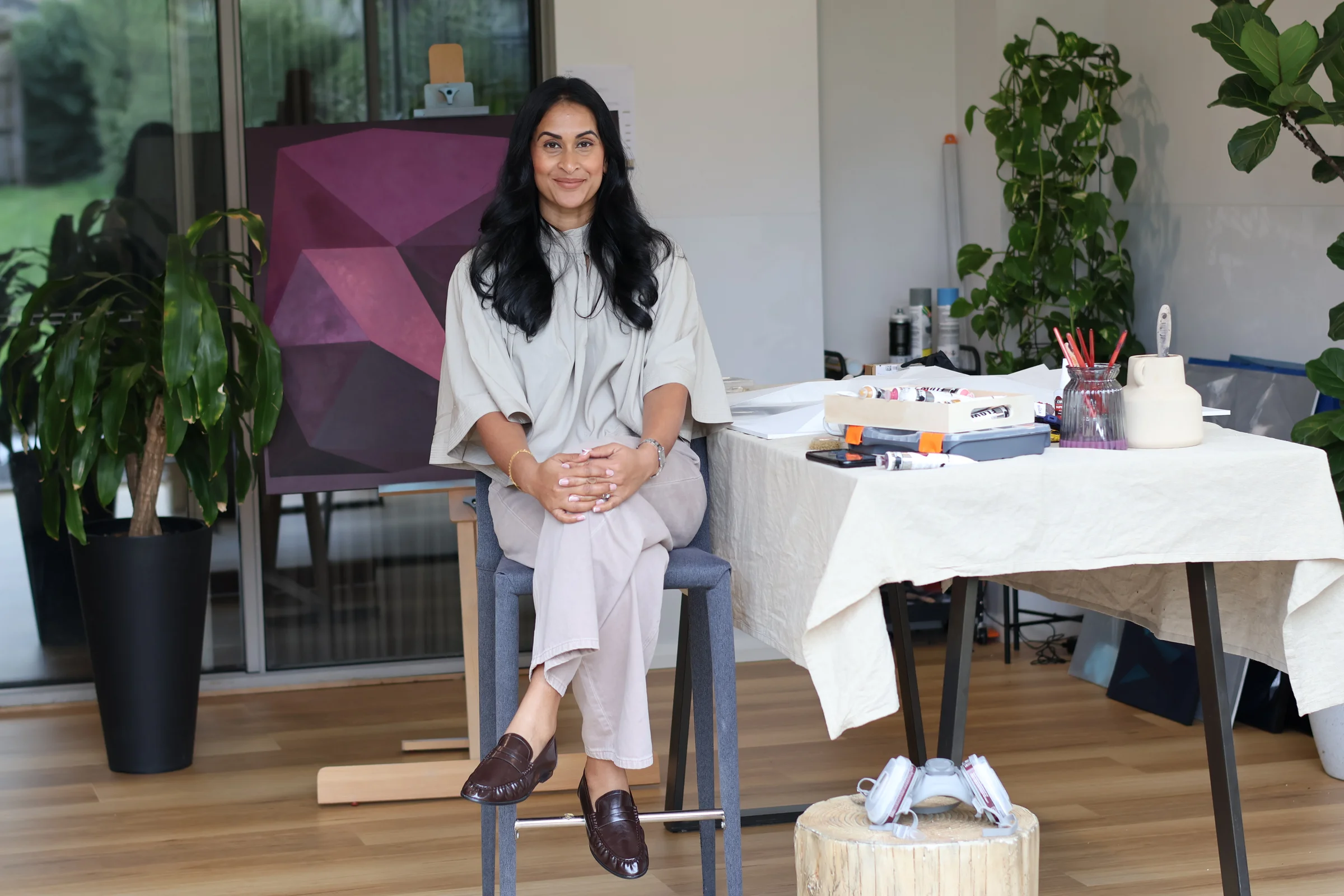 Kalani seated in her Melbourne studio beside a geometric relief artwork and painting materials