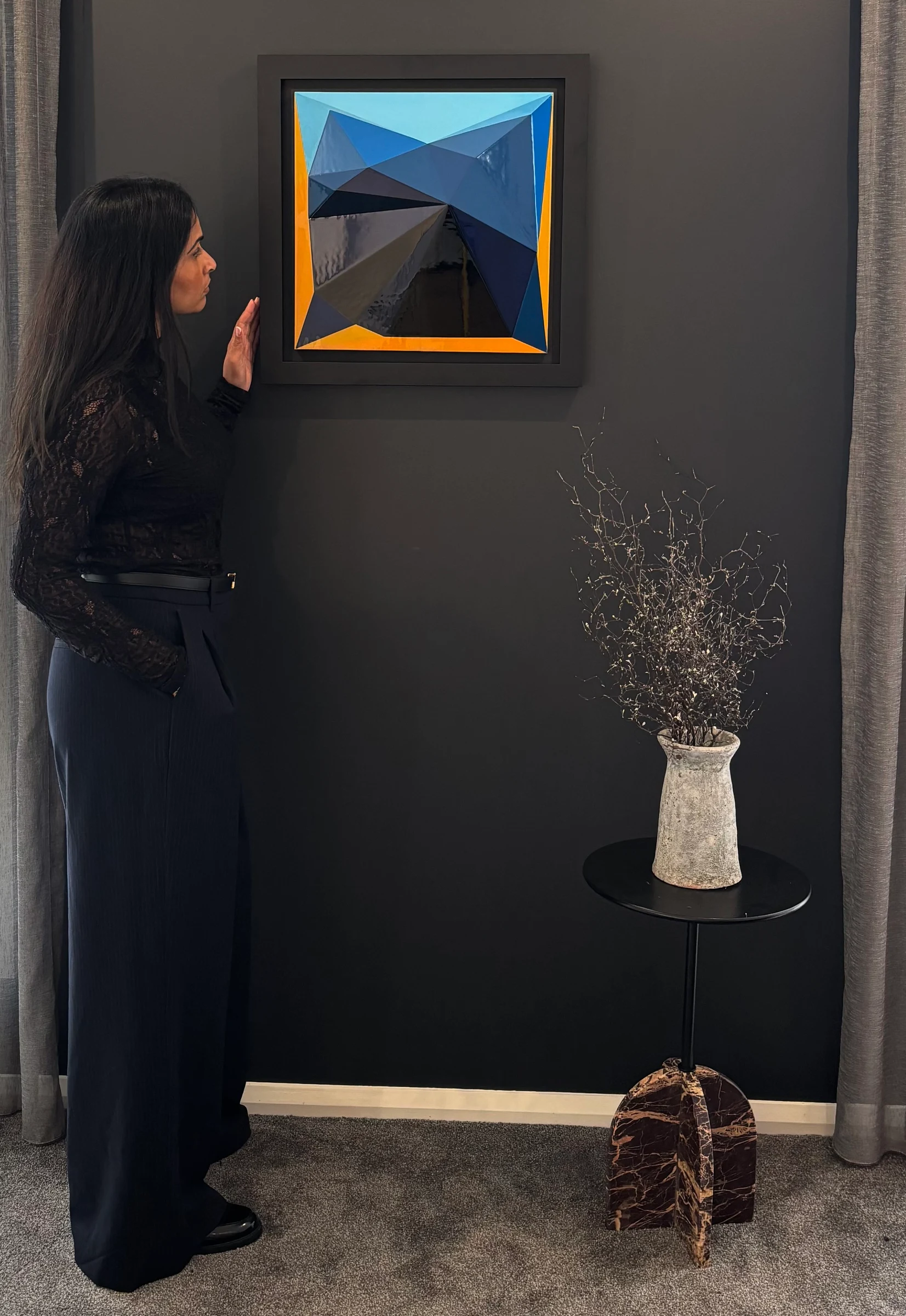 A woman standing beside Shallow Relief and Saturation on a dark wall between curtains