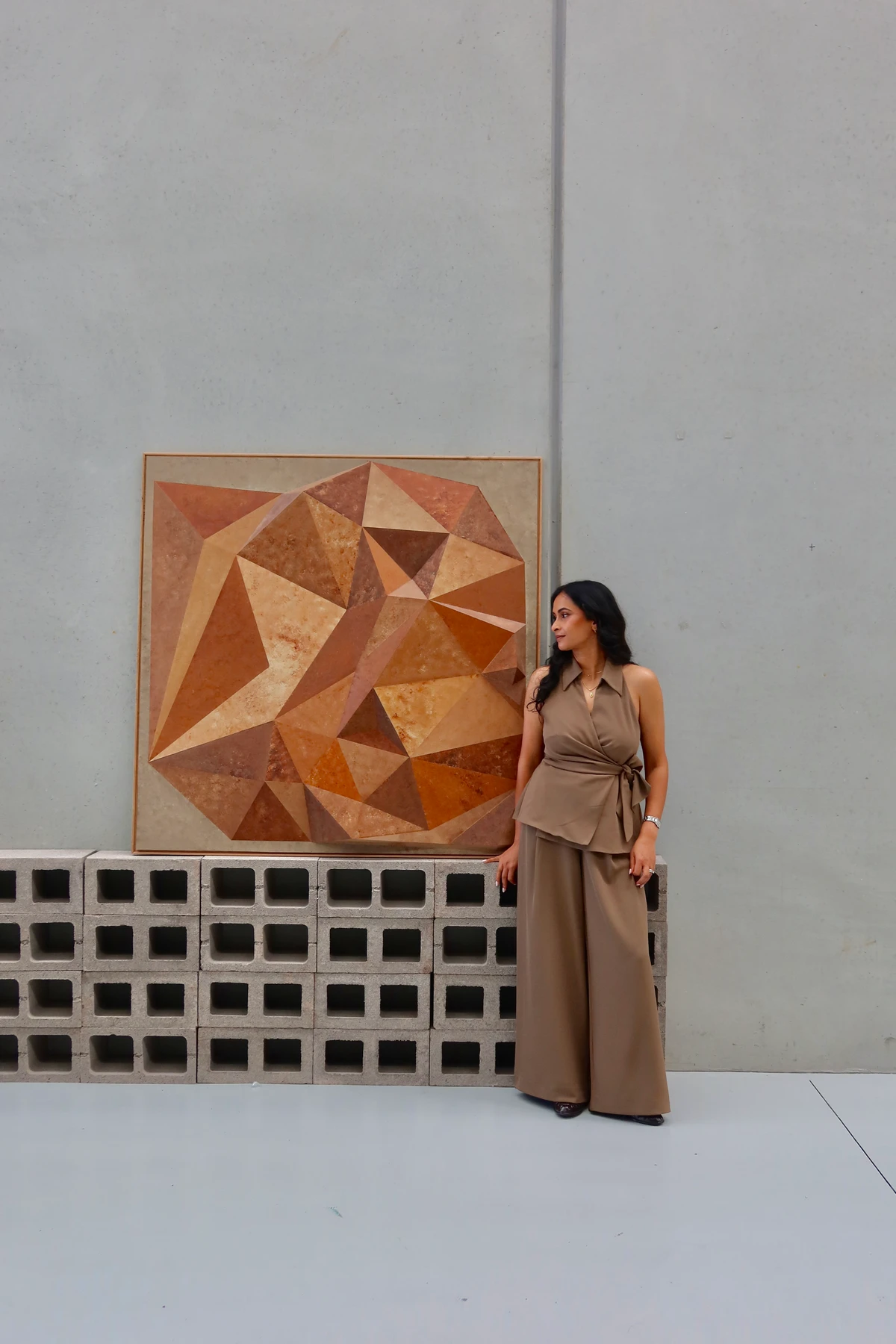 Artist standing beside the terracotta and ochre relief on a concrete block wall