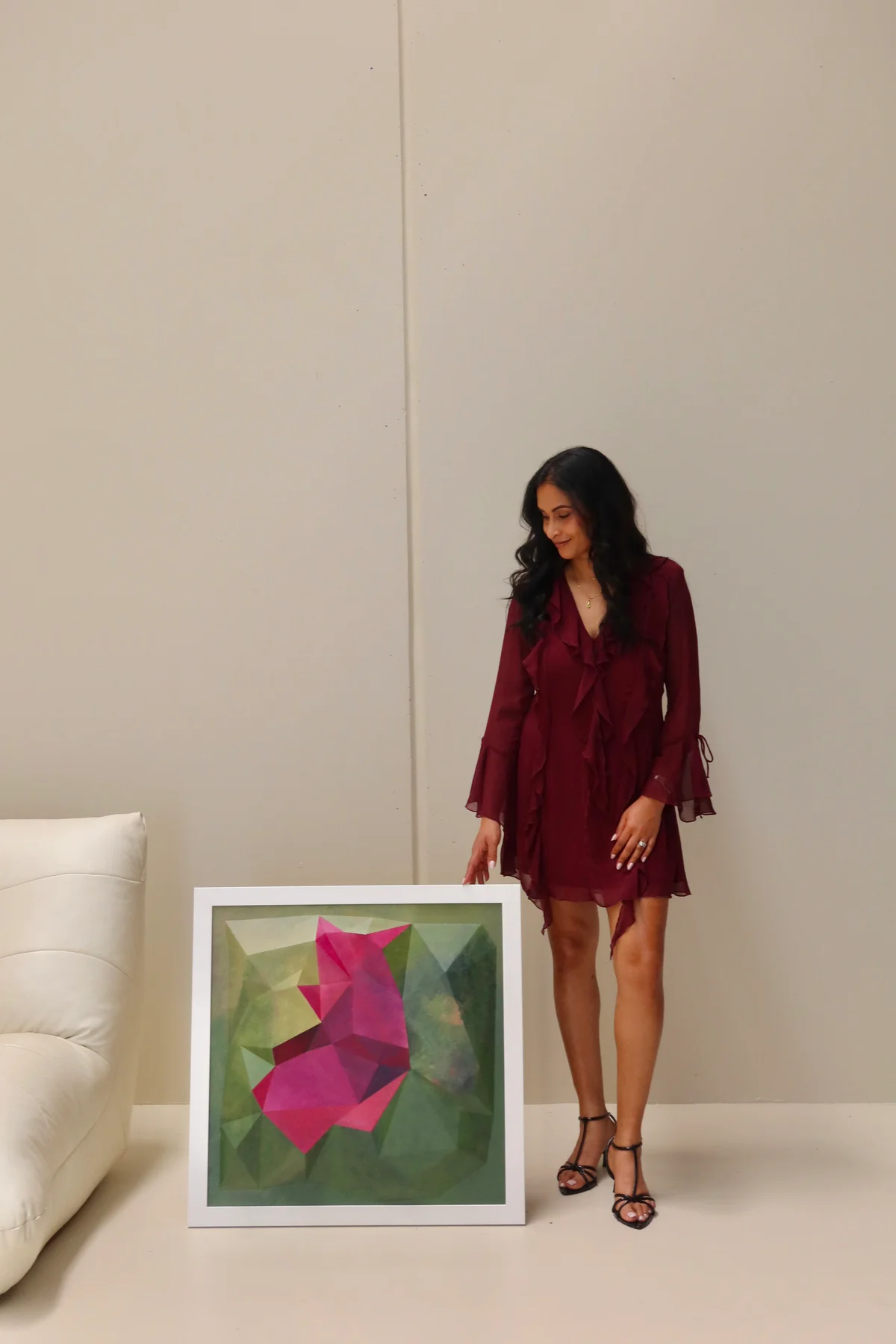 Framed magenta and green artwork on the floor beside a white sofa and a standing person